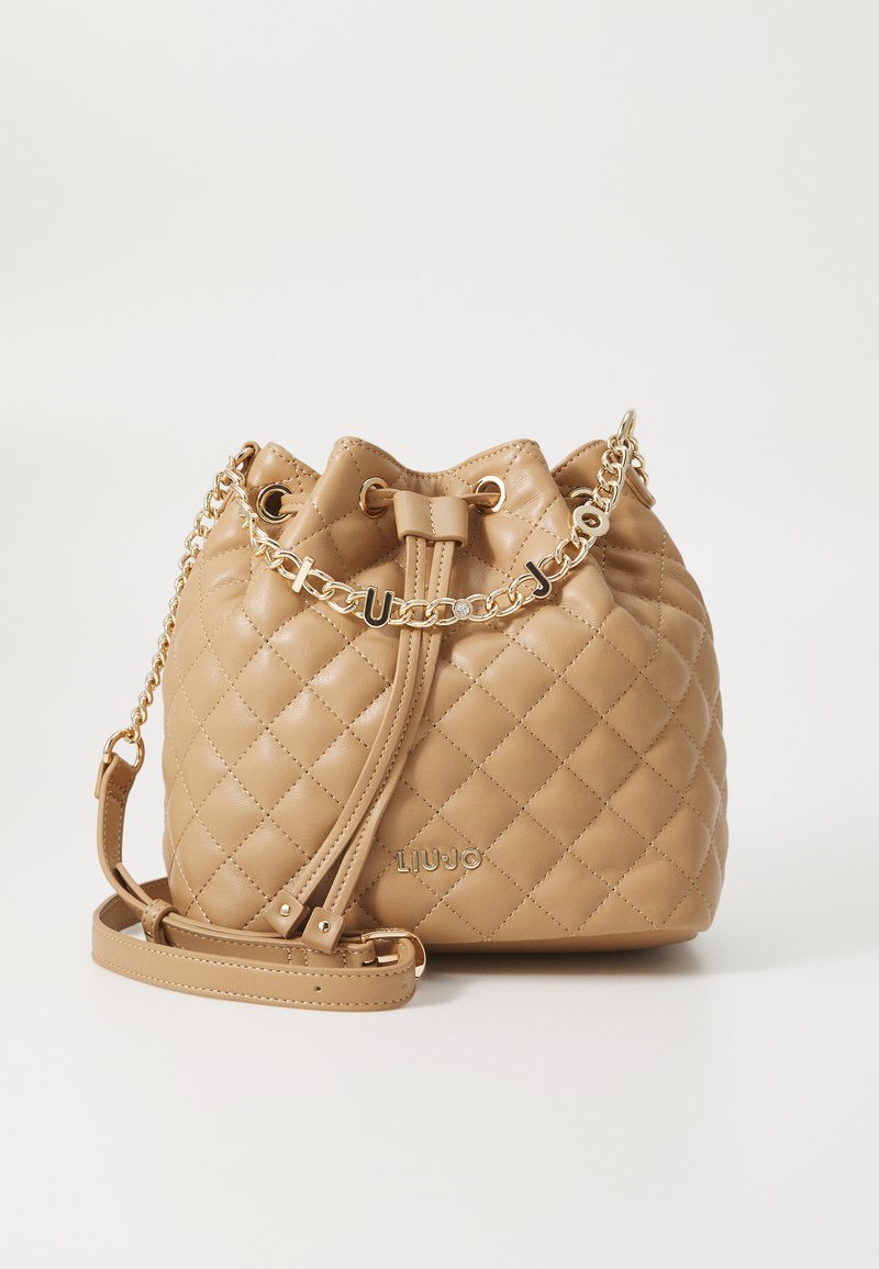 Beige gequilted emmer tas gemaakt van faux leer. Heeft een trekkoordsluiting, gouden kettingaccent en een verstelbare schouderband.
