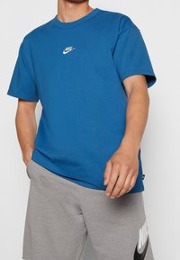 Blå bomulls t-shirt med korta ärmar, rund hals och vit Nike-logga centrerad på bröstet. Sparas med grå shorts med logga.