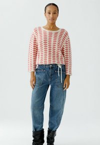 White sweater with red lip pattern, paired with blue high-waisted denim pants. The outfit features relaxed fit and subtle texture variations.