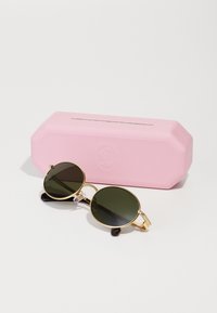 Gafas de sol redondas con lentes verde oscuro, montura de metal dorado y puntas de patilla negras, exhibidas junto a un estuche octogonal rosa.