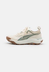 Scarpe da ginnastica beige con tomaia in rete traspirante, dettagli verdi, suola flessibile e un pattern di trazione pronunciato sulla suola in gomma marrone.