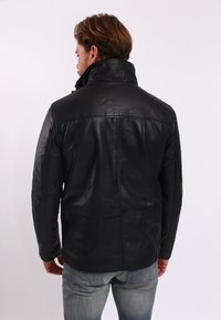 Svart läderjacka med hög krage, med en slät yta och detaljerad sömnad, visad bakifrån med grå jeans.