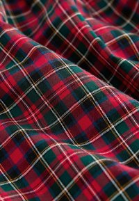 Tissu en tartan à carreaux rouge, vert, noir et blanc avec des plis diagonaux créant des ombres douces et de la texture.