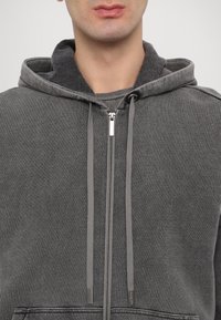 Grauer Reißverschluss-Hoodie mit Kordelzugkapuze, glatter Textur, Fronttaschen und silberner Reißverschlussbeschlägen. Einfaches und minimalistisches Design.