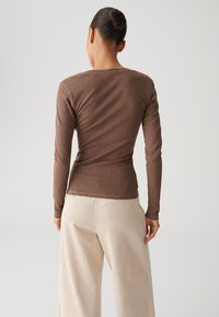 Brown long-sleeve top with a fitted silhouette, ribbed texture, and round neckline, paired with cream wide-leg ribbed pants.