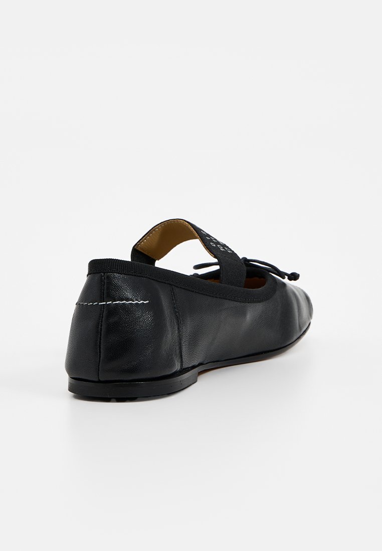 Ballerine in pelle nera con punta arrotondata, cinturino elastico e cuciture decorative. Texture liscia e design minimalista.