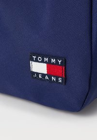 Tissu bleu marine avec un patch logo brodé Tommy Jeans affichant un design rectangulaire blanc, rouge et bleu marine.