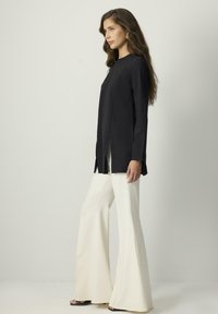 Maglietta nera a maniche lunghe con spacchi laterali, abbinata a pantaloni bianchi a gamba larga. Il tessuto sembra liscio, con una vestibilità sartoriale e un collo tondo.