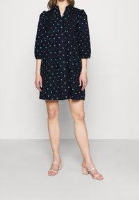 Mörkblå klänning med V-ringning, puffärmar och prickar. Tyget verkar lätt och har en avslappnad passform samt knapppdetaljer.