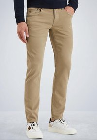 Pantalones ajustados color caqui hechos de una mezcla de algodón. Presentan cinco bolsillos, costuras visibles y una textura suave. Combinados con zapatillas blancas.