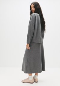 Grå, oversized sweater med lange ærmer, parret med en matchende lang nederdel. Sættet har en blød tekstur og er komplementeret af lyserøde sko.