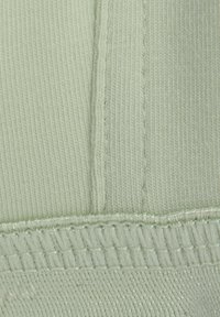 Tissu vert clair présentant une surface texturée avec de fins nervures, des coutures piquées et un ourlet lisse en bas.