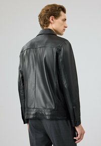 Zwart leren jack met een gladde textuur, voorzien van een standaard kraag, knoopmanchetten en een getailleerde pasvorm, getoond vanaf de achterkant.