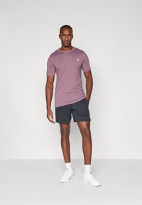 T-shirt de sport bordeaux à manches courtes, assorti avec des shorts foncés. Présente un logo discret sur la poitrine et une coupe décontractée.