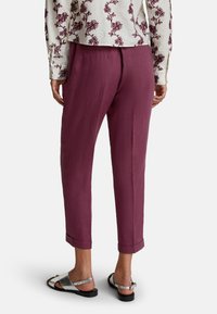 Pantalons en lin bordeaux avec une coupe décontractée, ourlets retroussés et poches latérales. Associés à des sandales plates argentées et un chemisier à motif floral.
