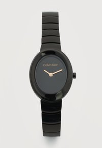 Μαύρο ρολόι χειρός Calvin Klein με οβάλ καντράν, μίνιμαλ σχεδιασμό, χρυστά δείκτες ώρας και λεπτών, και γυαλιστερό διαιρεμένο λουράκι σε ανοικτό φόντο.