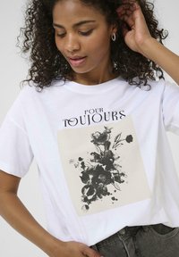 T-shirt en coton blanc avec un graphique floral carré en noir et gris, accompagné du texte "POUR TOUJOURS" au-dessus du design. Manches courtes.