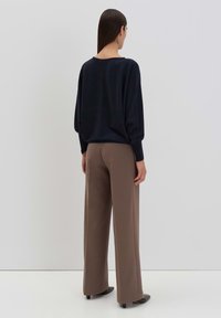 Marineblauer Pullover mit lockerer Passform und langen Ärmeln, kombiniert mit beigefarbenen weit geschnittenen Hosen. Glatte Stofftextur; minimalistisches Design, neutrale Farbpalette.