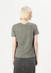 Olivgrünes T-Shirt mit kurzen Ärmeln und rundem Ausschnitt, mit verblichenem Design und aufgerollten Ärmeln, kombiniert mit einem dunklen Jeansrock mit Gesäßtaschen.