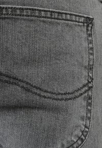 Tessuto in denim grigio che mostra un primo piano di una tasca posteriore. Presenta un taglio pulito con cuciture visibili e una leggera texture. Nessun abbellimento presente.