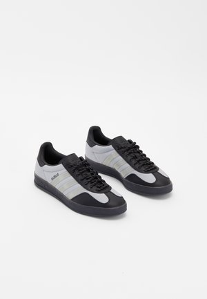 Par af Adidas Gazelle sneakers i sort og grå med sorte snørebånd, der viser sidebranding og tre karakteristiske striber på hver sko.