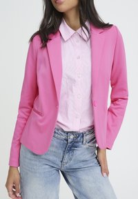 Pinker Blazer aus glattem Stoff, mit Reverskragen, Single-Button-Verschluss und vorderen Taschen, über einem gestreiften Hemd getragen.