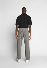 Černé polo tričko s krátkým rukávem a volným střihem, doplněné vysokými kalhotami s kostkovaným vzorem a širokými nohavicemi, a bílými teniskami.