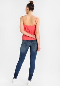 Top rojo sin mangas con tirantes finos y cintura ceñida, combinado con jeans ajustados de color azul con un lavado claro y un ligero deshilachado en el dobladillo.