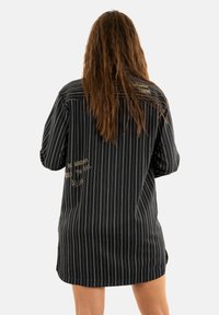 Abito a camicia a righe bianche e nere con vestibilità rilassata, dotato di testo ricamato sulla schiena e sul davanti. Maniche lunghe, texture morbida.