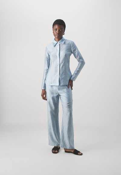 Chemise bleu clair à boutons associée à un pantalon large assorti. Les deux vêtements présentent un tissu souple et texturé ainsi qu'un design de col classique.