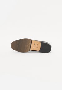 Black leather shoe sole with a textured rubber base and vertical grooves. Brownish inner lining with printed branding detail.