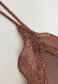 Bralette en dentelle marron avec broderie florale et tissu côtelé, doté de fines bretelles doubles sur un fond clair.