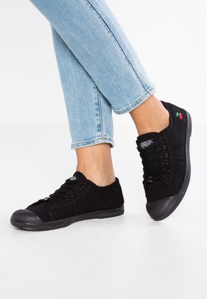 Zwarte canvas sneakers met rubberen neuskap, vetersluiting en geborduurd kersdetail aan de zijkant. Gecombineerd met lichtblauwe jeans.