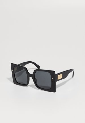 Black oversized sunglasses with square frames, grey tinted lenses, and gold accents on the temples. Smooth plastic finish with metallic detail.
