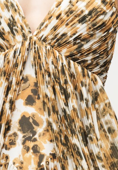 Κοντινό πλάνο σε καφέ, μαύρο και λευκό ύφασμα με animal print και πιέτες, με λεπτομέρεια φιόγκου στη μέση μπροστά ενός φορέματος.