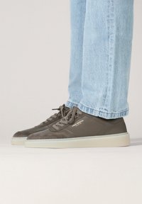 Szare sneakersy wykonane z zamszu i skóry, wyposażone w gumową podeszwę, okrągły nosek oraz sznurowadła w tym samym odcieniu. Noszone z jasnoniebieskimi podwiniętymi jeansami.