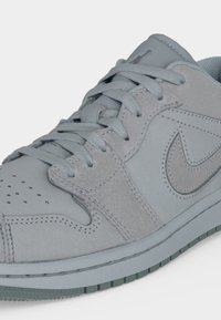 Ανοιχτό γκρι αθλητικό παπούτσι με πάνελ από σουέτ και δέρμα, κεντημένο λογότυπο Nike swoosh στο πλάι, επίπεδα κορδόνια και διάτρητα στην περιοχή των δαχτύλων.