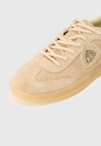 Μπεζ αθλητικό παπούτσι από σουέντ με στρογγυλεμ�ένη μύτη, λαστιχένια σόλα και σχέδιο με κορδόνια. Διαθέτει υφασμάτινο ένθετο με γεωμετρικό μοτίβο.