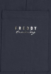 Pantalones de chándal azul marino oscuro con un bolsillo prominente que presenta "FREDDY" en letras metálicas en negrita y "training" en estilo cursivo debajo.