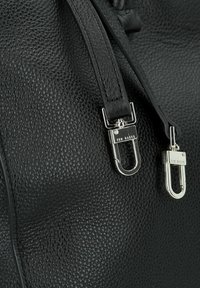 Bolso de cuero negro con textura, equipado con herrajes plateados, doble cierre y correas suaves. Logo distintivo de la marca visible en los herrajes.