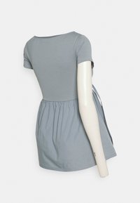 Camiseta de algodón gris con cuello redondo, mangas cortas y cintura fruncida. Presenta un detalle de lazo en la parte posterior y una textura suave.