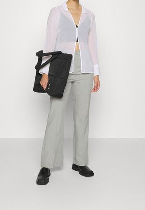 Camicia bianca traslucida con colletto, pantaloni grigi a vita alta e una borsa a tracolla nera in tessuto. Le scarpe nere completano l'outfit.