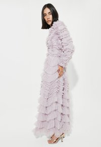 Lavendelfärgad klänning med lager av volanger, långa ärmar och en åtsittande bodice. Mixad med guldklacksandaler med en dekorativ spänne.