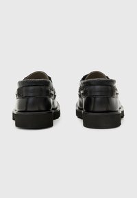 Zapatos de cuero negro con un respaldo texturizado y estampado, punta redonda y suela de goma de perfil bajo. Presentan un detalle de correa de cuero en cada lado.