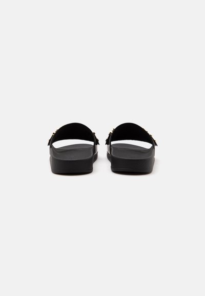 Paire de sandales noires à larges brides avec des boucles dorées, vues de dos sur fond blanc uni.