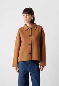 Hnědá bunda z vlněné směsi s límcem, předními knoflíky a volným střihem. Má dlouhé rukávy a zkrácený design.