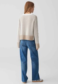 Strickpullover mit vertikalen Streifen in Creme und Beige, hat einen verkürzten Schnitt, weite Ärmel und gerippte Details am Saum. Kombiniert mit blauen Jeans.