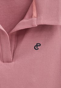 Piké i mjuk, ribbad rosa tyg med en vikbar krage. Har en liten marinblå logotyp på bröstet som framhäver textur och färgkontrast.