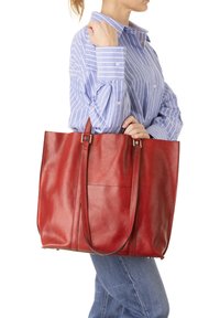 Borsa tote in pelle rossa con texture liscia, due manici lunghi e una tasca frontale. La borsa ha una forma rettangolare e una costruzione robusta.