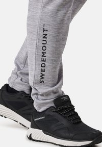 Graue Sporthose mit vertikalem "SWEDEMOUNT"-Text und schwarzen leichten Turnschuhen mit weißer Sohle und strukturierten Akzenten.